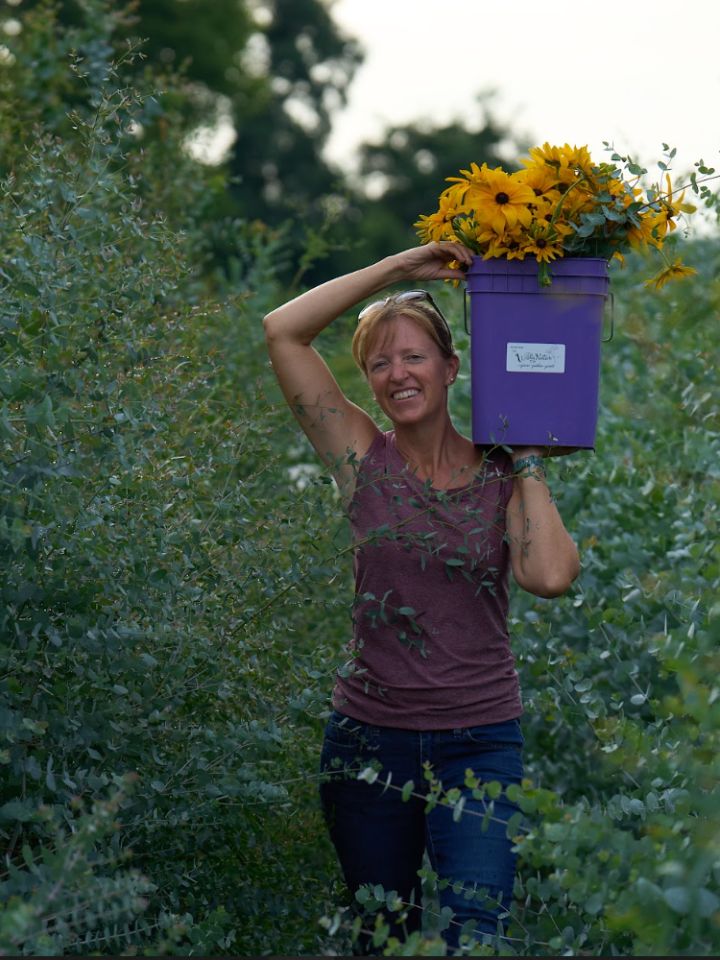 Liza holding a purple bucket on her shoulder, filled with yellow flowers