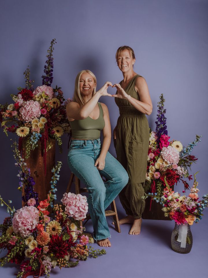 Lizzy and Liza in front of a purple backdrop with flowers.