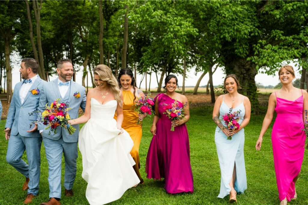 Bride and Groom walk smiling with wedding party in bright colors holding flowers.