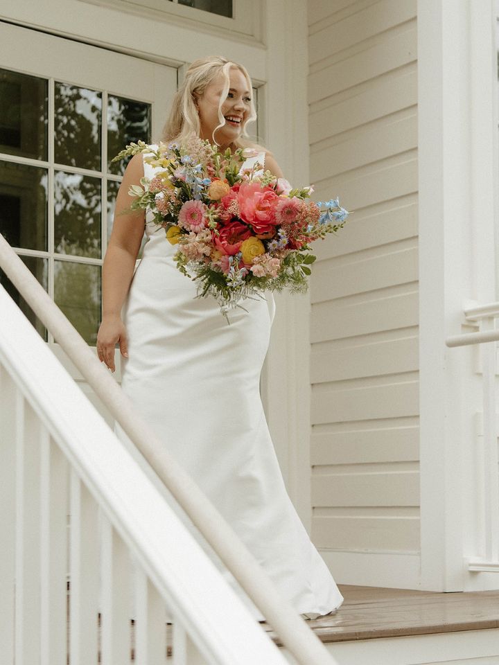 Bride stands on front steps of Kent Island Resort with spring pastel bouquet.