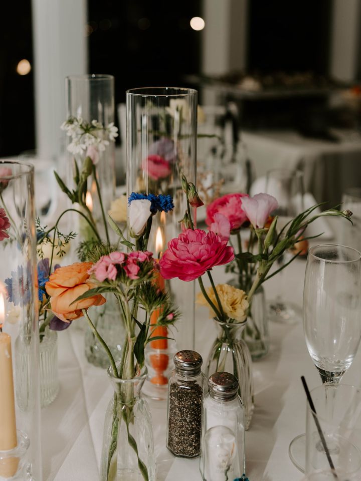 Scattered bud vases in bright and soft spring florals on a round guest table with candles.