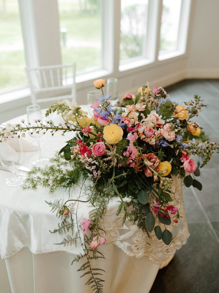 A low arrangement sits on the front edge of a sweetheart table.