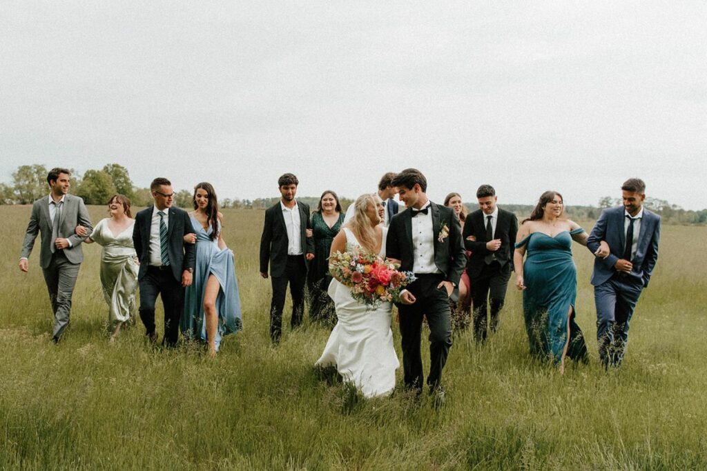 Bride and Groom lead their wedding party through a field.