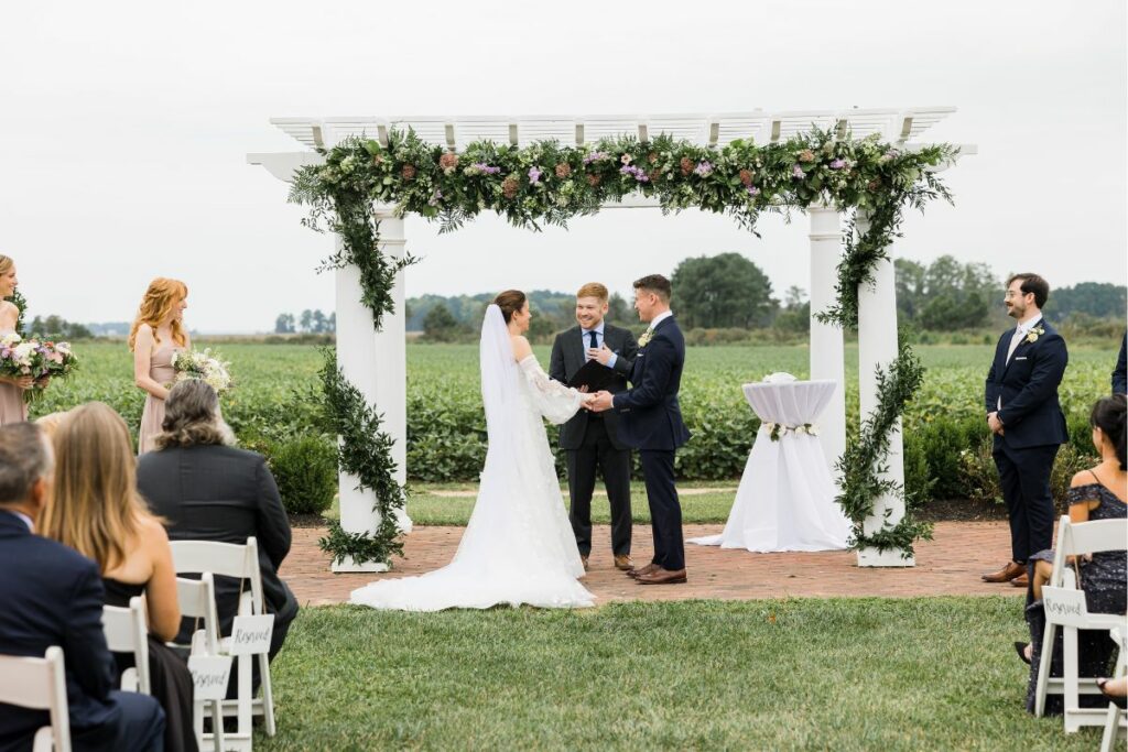 Bride and Groom say their vows under a white pergola decorated by a Kent Island Resort florist.