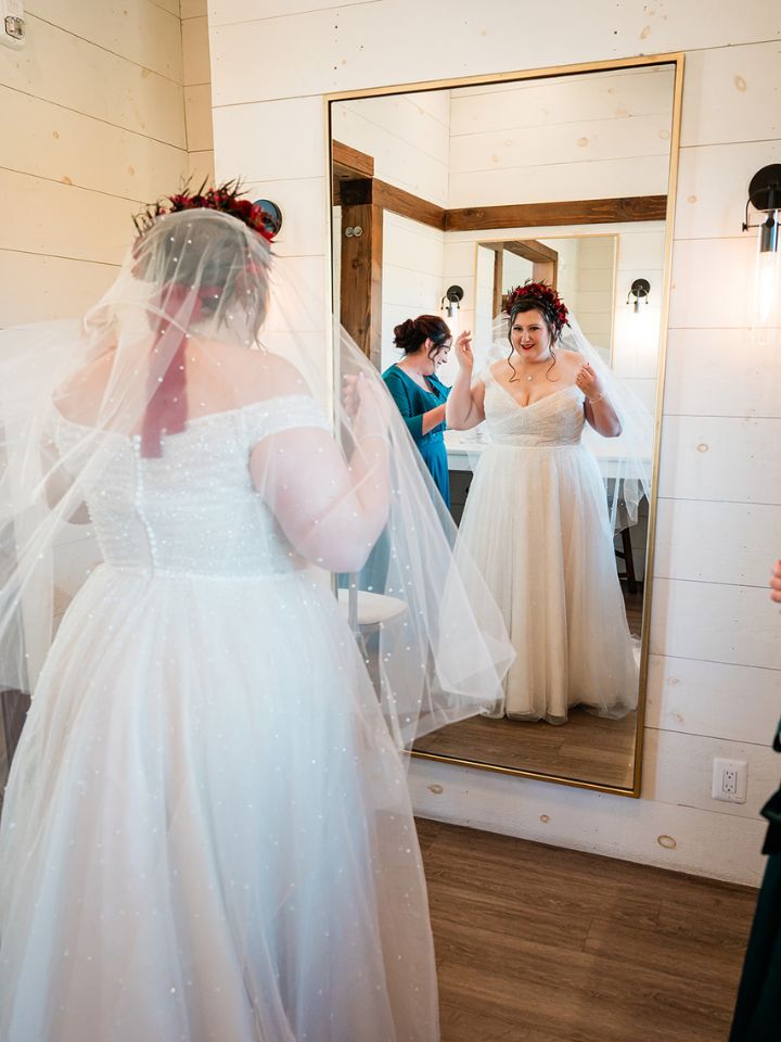 Bride adjusts her veil and flower crown in an oversized mirror.