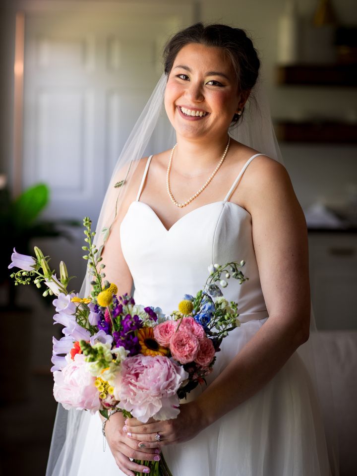 Bride holds her bouquet of colorful florals and smiles at the camera.