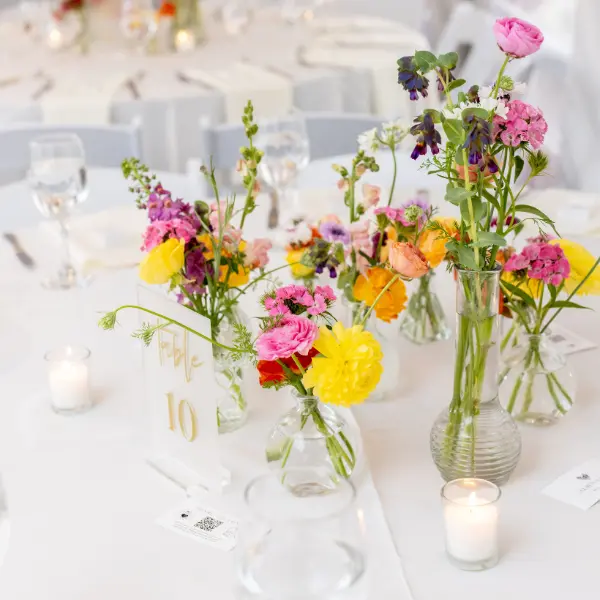 Scattered floral vases on a round table by Wildly Native Flower Farm