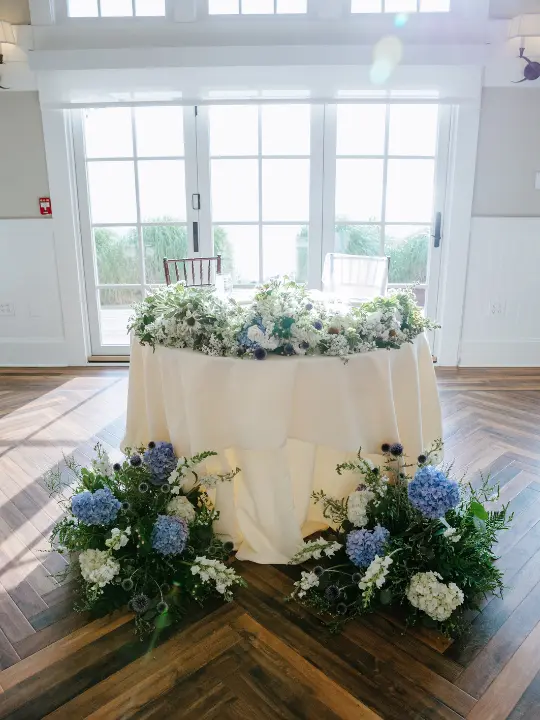 sweetheart-table-with-blue-florals White sweetheart table with florals at the base and on top by Wildly Native Flower Farm